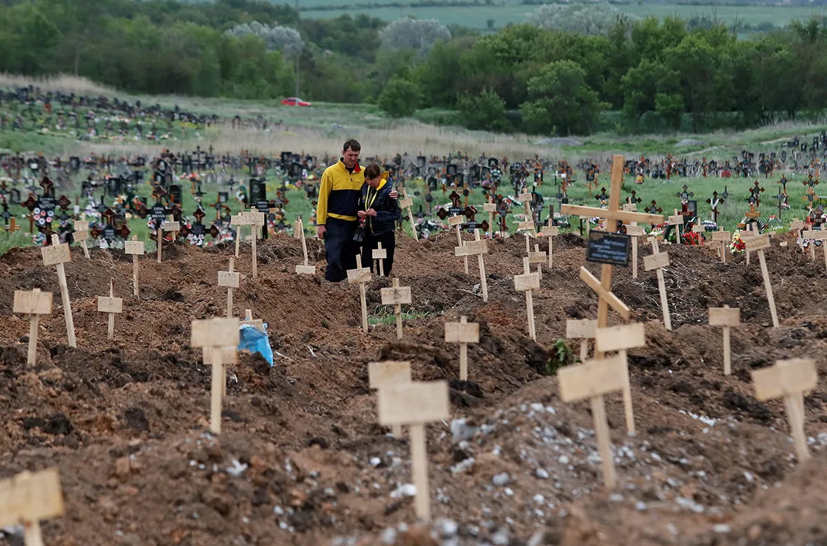 Люди у могил, вырытых в течение войны, в поселке Старый Крым под Мариуполем, Украина, 22 мая 2022 года