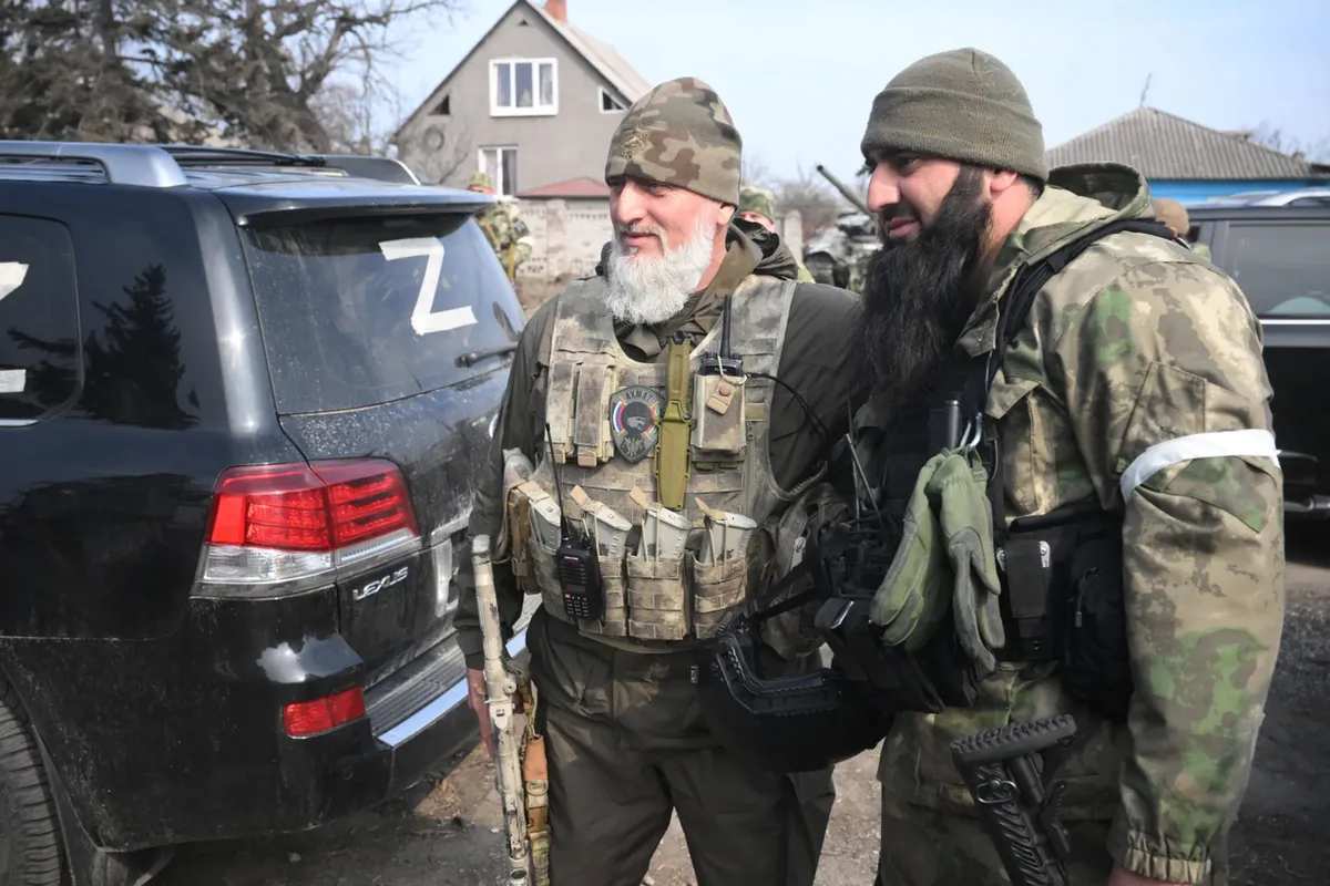 Adam Delimkhanov (left) posing against the background of a clearing operation of Mariupol's Left Bank district 
